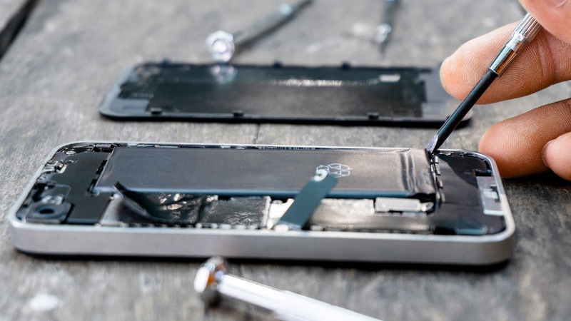 A hand uses a tool to inspect the inside of a mobile phone that has had its back case removed